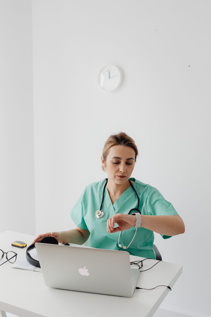 A female doctor checks the time during an online consultation at her desk.